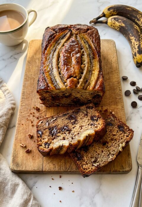 Gordon Ramsay banana bread sliced on a wooden board showing chocolate chips and pecans inside with caramelised banana on top
