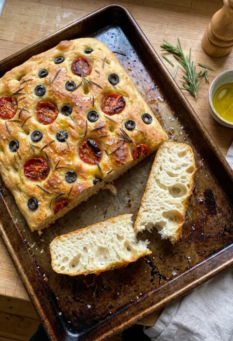 Gordon Ramsay focaccia bread with olives tomatoes and rosemary on a baking tray showing airy crumb