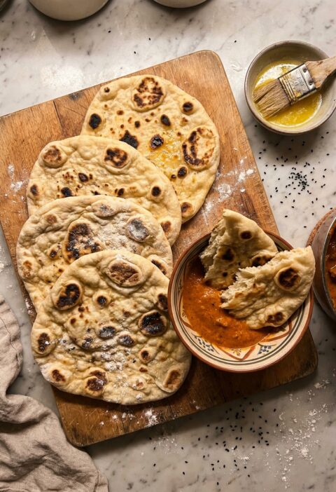 Gordon Ramsay naan bread with charred bubbles on a wooden board with curry and melted ghee