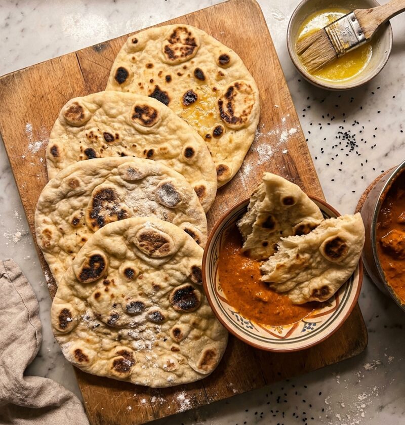 Gordon Ramsay naan bread with charred bubbles on a wooden board with curry and melted ghee
