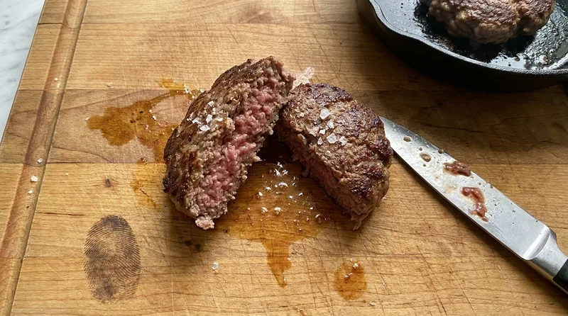 Thick homemade burger patty cut in half showing a browned crust and juicy pink centre from a proper 80/20 meat blend