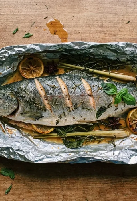Gordon Ramsay baked salmon, a whole scored fish on a bed of herbs in opened foil with caramelised lemon, star anise and lemongrass