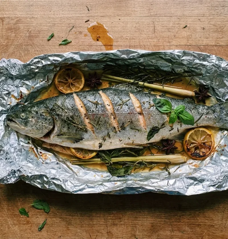 Gordon Ramsay baked salmon, a whole scored fish on a bed of herbs in opened foil with caramelised lemon, star anise and lemongrass