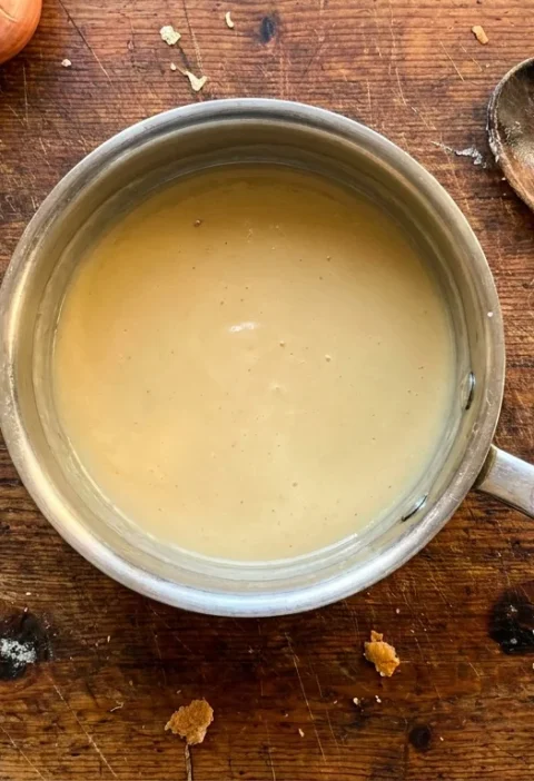 Gordon Ramsay beurre blanc lemon butter sauce in a stainless steel saucepan with shallots and lemon on a wood table