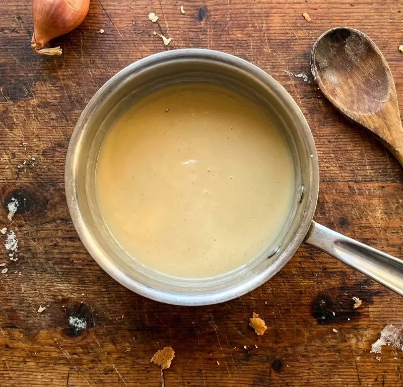 Gordon Ramsay beurre blanc lemon butter sauce in a stainless steel saucepan with shallots and lemon on a wood table