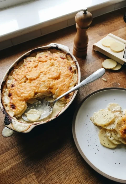 Gordon Ramsay dauphinoise potatoes in a gratin dish with golden Cheddar crust and a portion served on a plate