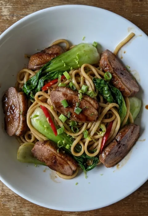 Gordon Ramsay duck stir fry with egg noodles, pak choi, red chilli and spring onions in a white bowl