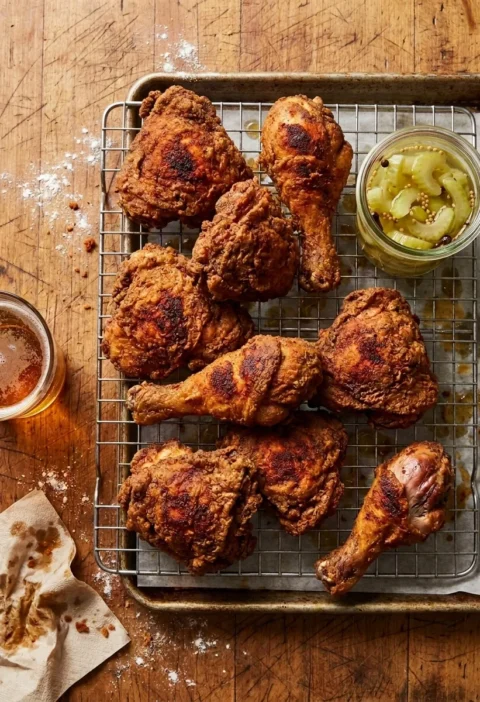 Homemade buttermilk fried chicken thighs and drumsticks with blistered spiced flour crust on a wire rack with pickled celery