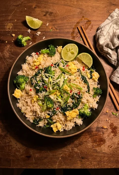 Gordon Ramsay fried rice with broccoli scrambled egg and spring onions in a dark bowl on a wood table