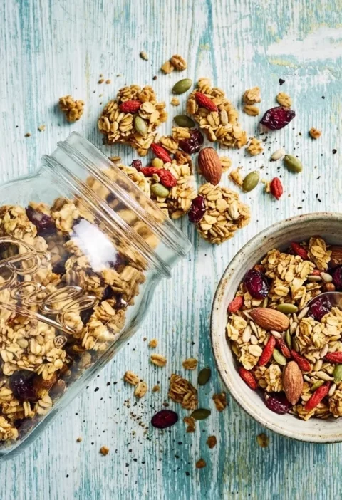 Gordon Ramsay homemade granola with oat clusters almonds pumpkin seeds goji berries and cranberries in a glass jar and speckled bowl