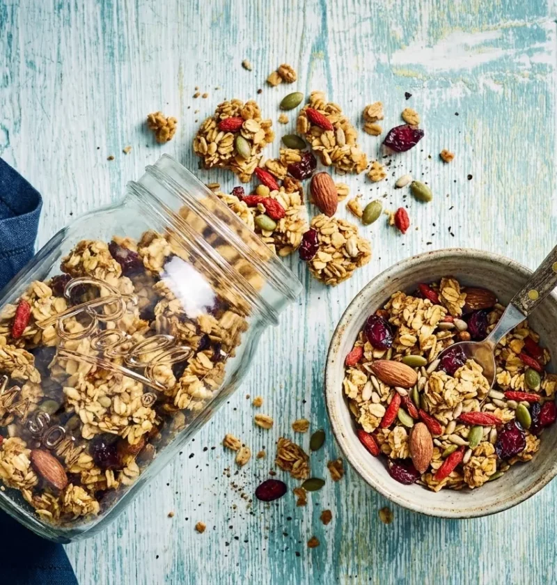 Gordon Ramsay homemade granola with oat clusters almonds pumpkin seeds goji berries and cranberries in a glass jar and speckled bowl