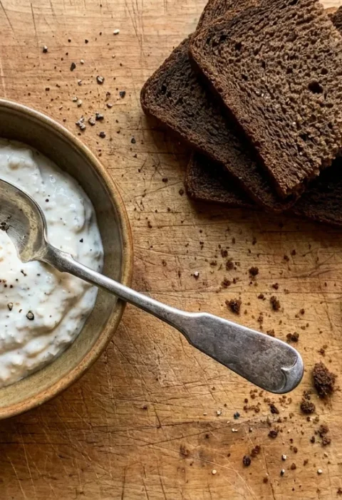 Gordon Ramsay horseradish sauce in a ceramic bowl with cracked black pepper, pumpernickel bread and smoked salmon on a wood table