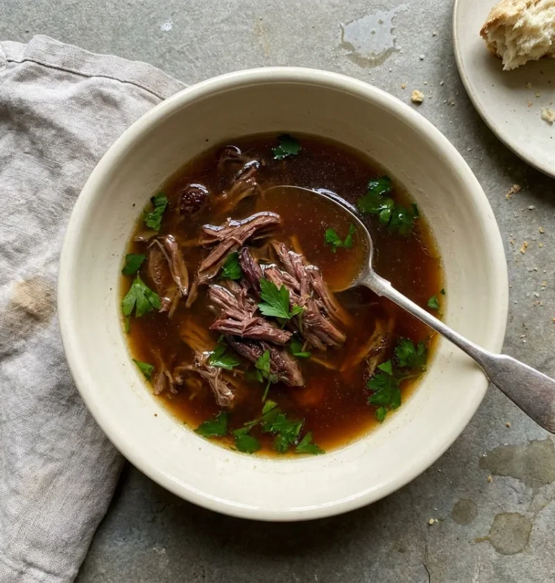 Gordon Ramsay oxtail soup, a clear deep-brown beef broth with shredded oxtail meat and parsley, served with soda bread