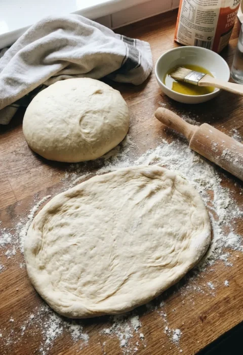 Gordon Ramsay pizza dough risen and stretched on a floured wooden worktop