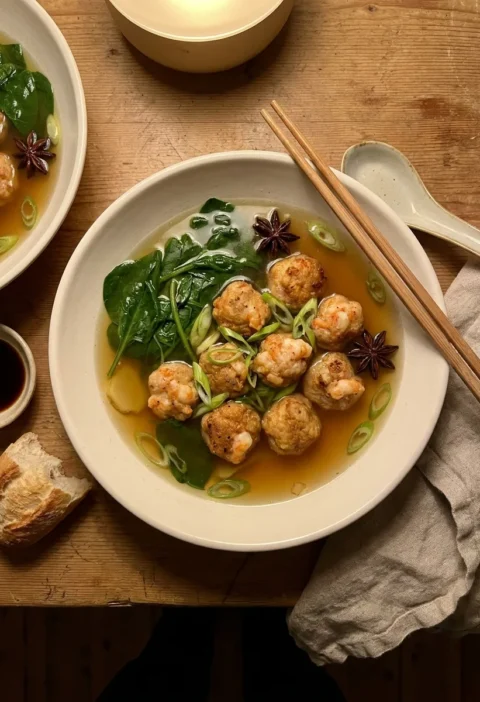 Pork and prawn meatballs in aromatic star anise broth with wilted spinach spring onion and chopsticks in a white bowl