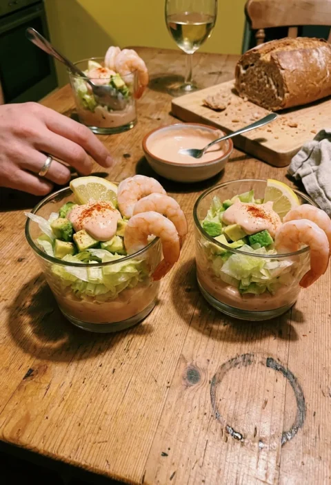 Prawn cocktail served in glasses with layers of Marie Rose sauce shredded iceberg lettuce diced avocado and poached prawns with cayenne pepper and lemon