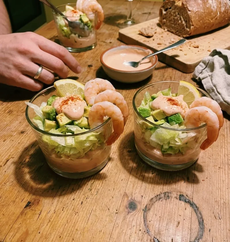 Prawn cocktail served in glasses with layers of Marie Rose sauce shredded iceberg lettuce diced avocado and poached prawns with cayenne pepper and lemon