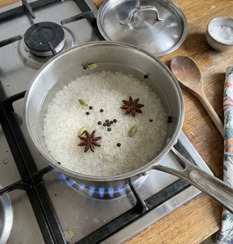 Basmati rice in a saucepan with cardamom pods and star anise on a gas hob ready to cook