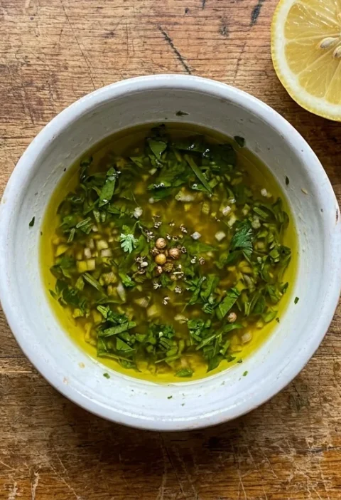 Gordon Ramsay sauce vierge in a white ceramic bowl with herb strips and crushed coriander seeds in olive oil on a wood table