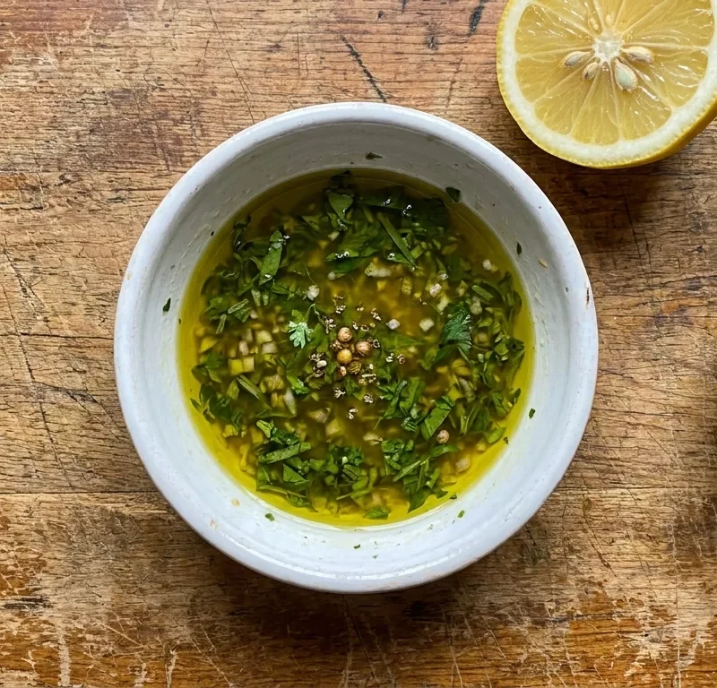 Gordon Ramsay sauce vierge in a white ceramic bowl with herb strips and crushed coriander seeds in olive oil on a wood table