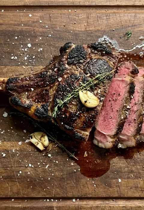 Gordon Ramsay tomahawk steak, seared and sliced to show a medium-rare pink centre, on a wooden board