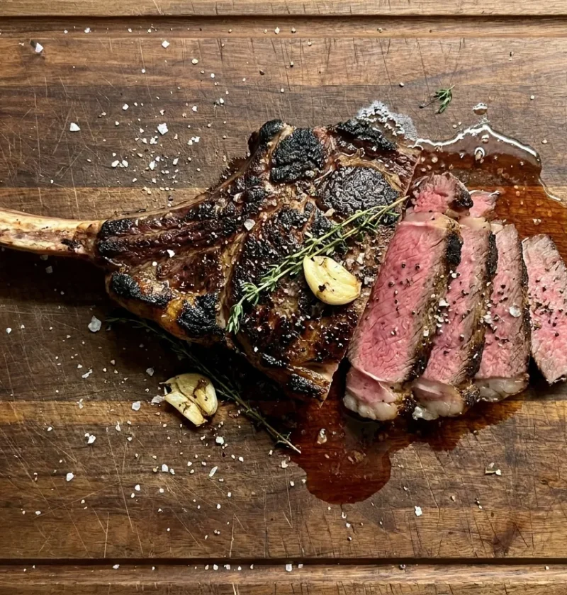 Gordon Ramsay tomahawk steak, seared and sliced to show a medium-rare pink centre, on a wooden board