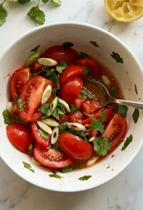 Gordon Ramsay tomato salsa: chunky halved plum tomatoes with diagonal spring onion slices and coriander in a white bowl, with sesame oil bottle, hot sauce and squeezed lemon