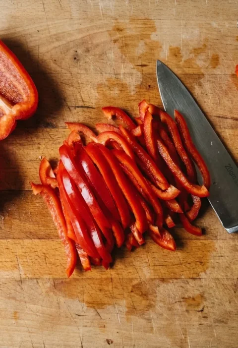 Red bell pepper cut into julienne strips on a board with the seed core removed, Gordon Ramsay method