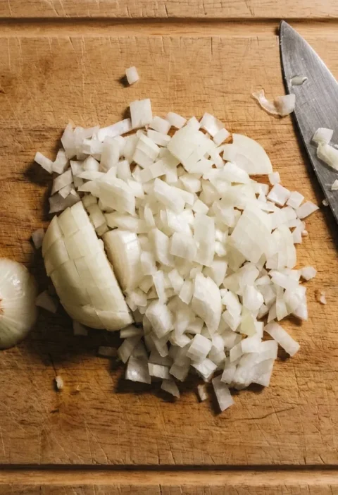 Finely diced onion on a wooden board with a chef knife and the root offcut, Gordon Ramsay method