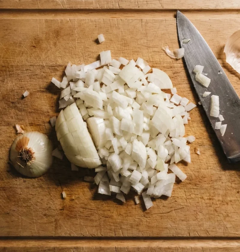 Finely diced onion on a wooden board with a chef knife and the root offcut, Gordon Ramsay method