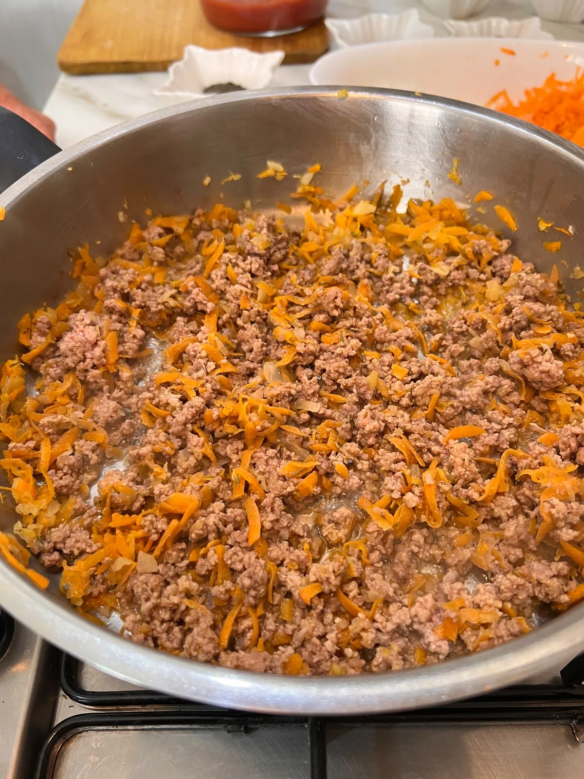 Mince cooking with grated carrot and onion in a stainless steel pan on a gas hob