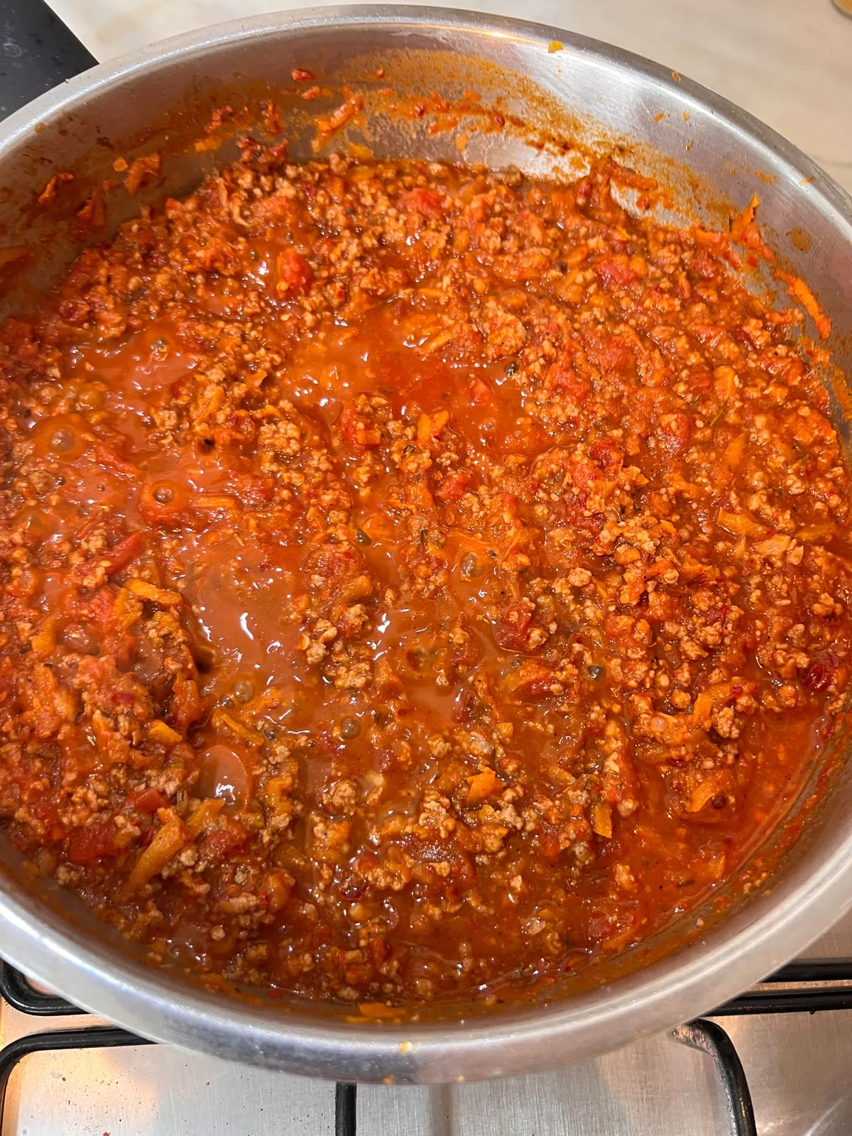Thick red bolognese sauce simmering in a stainless steel pan, made with harissa instead of wine