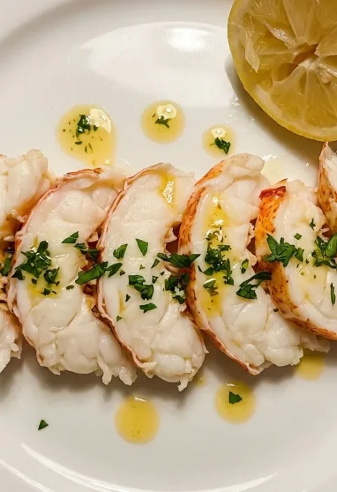 Gordon Ramsay butter poached lobster sliced on a white plate with golden herb butter and parsley