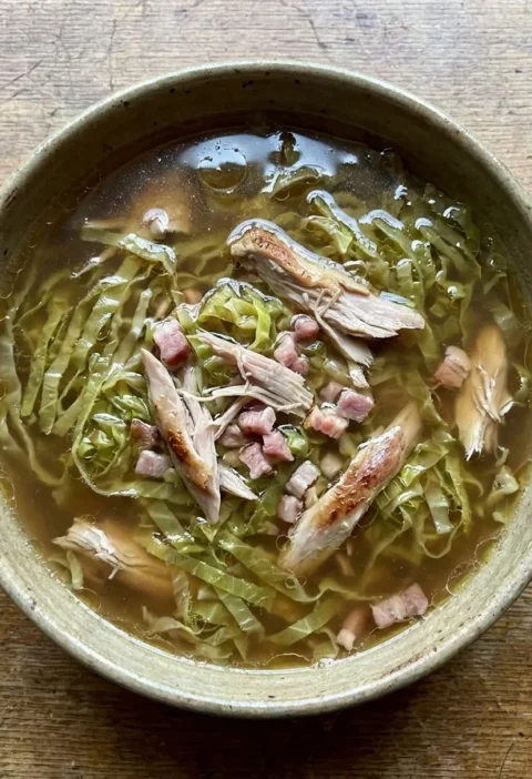 Gordon Ramsay cabbage soup with shredded Savoy cabbage and pulled rabbit meat in a clear brown broth