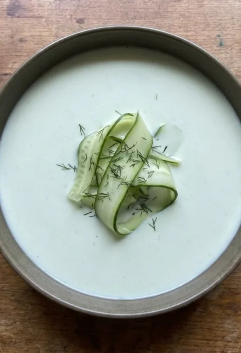Gordon Ramsay chilled cucumber soup, pale and smooth in a dark bowl, topped with folded cucumber ribbons and dill fronds