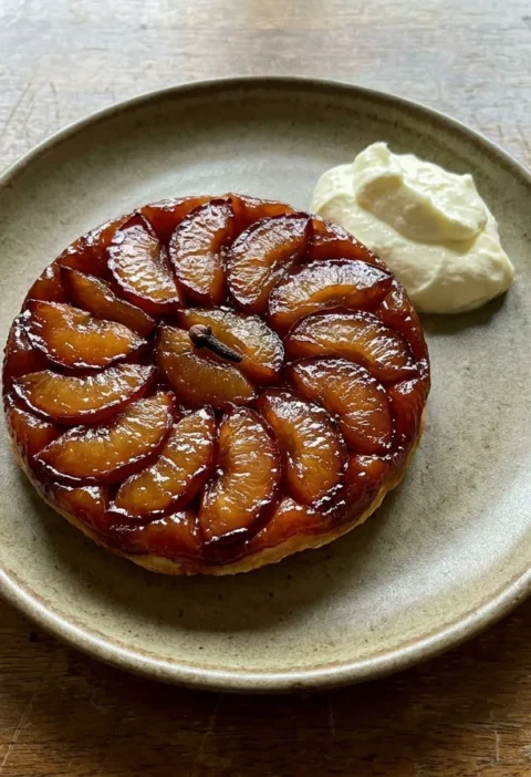Gordon Ramsay plum tart turned out upside down with caramelised plum slices on top and a whole clove in the centre