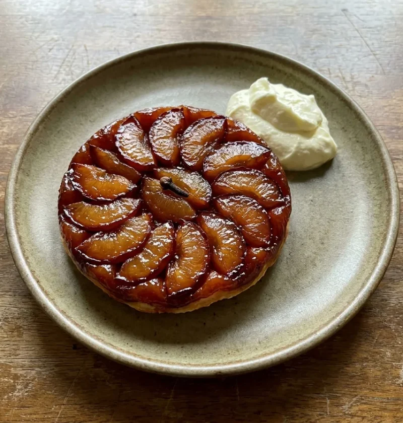 Gordon Ramsay plum tart turned out upside down with caramelised plum slices on top and a whole clove in the centre