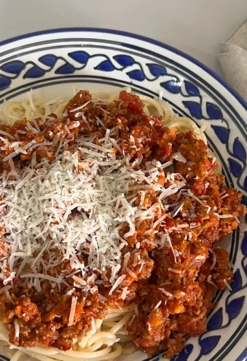 Gordon Ramsay spaghetti bolognese served in a blue patterned bowl, topped with grated Parmesan
