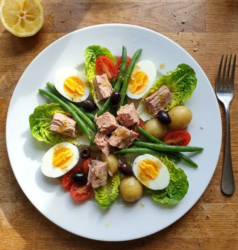 Gordon Ramsay tuna niçoise salad with tinned tuna, halved boiled eggs, green beans, new potatoes, black olives and baby gem lettuce on a white plate